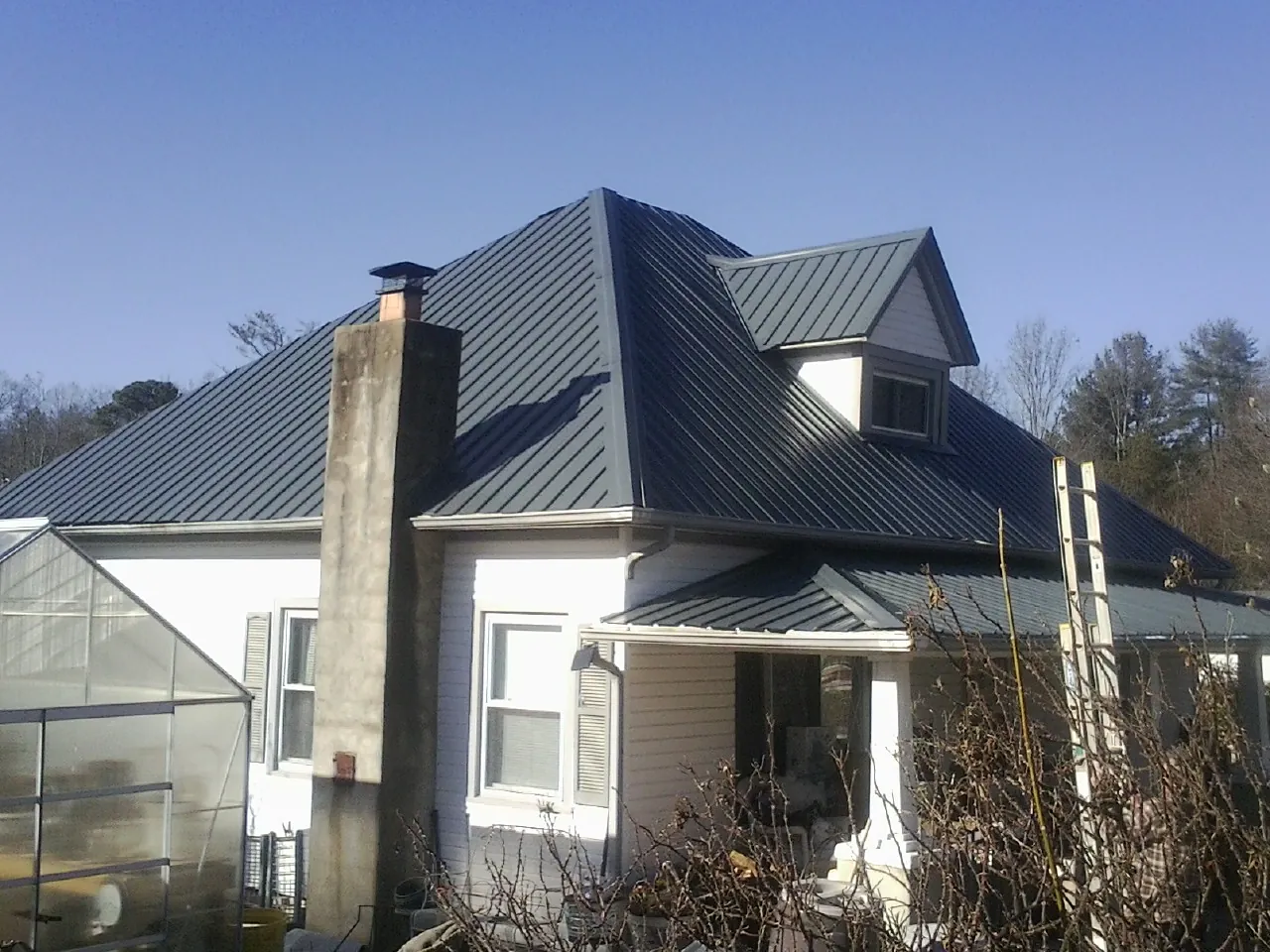 Dark blue standing seam metal roof on a white farmhouse with dormer — Slate & Tile Roof Repair by Roofing Brothers in Waupun