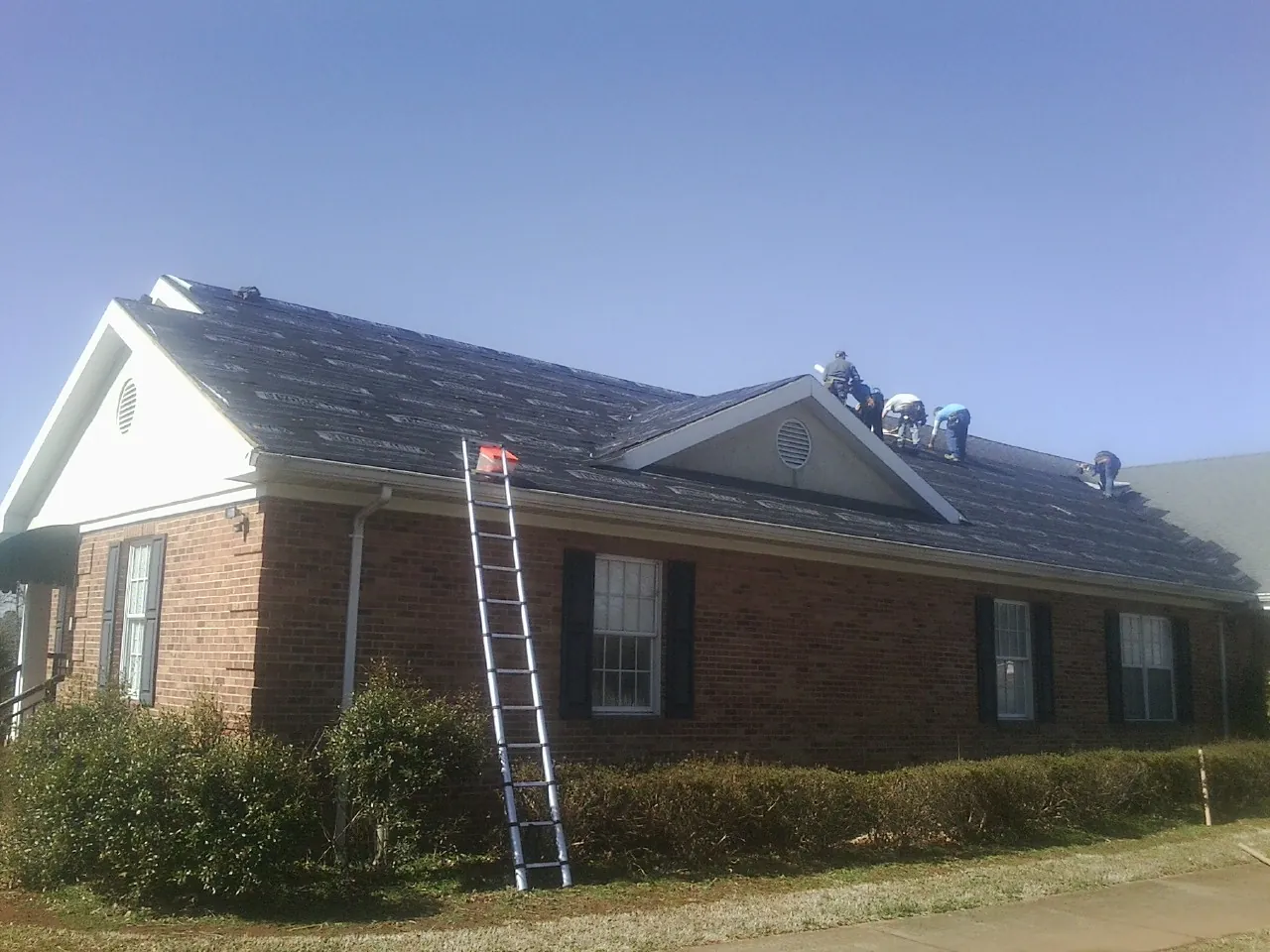 Crew tearing shingles off a brick ranch roof with a ladder set — Emergency Roof Repair work by our crew in Waupun