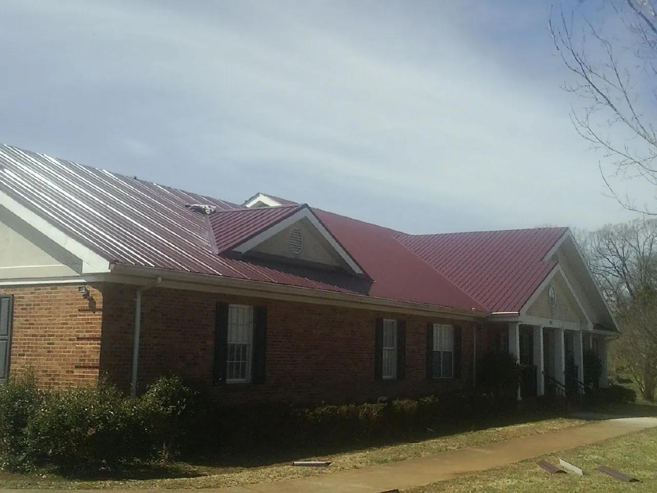 Red metal roof with gabled entries on a long brick building, from a Hail Damage Roof Repair job in Waupun
