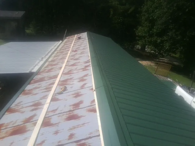 Old rusted panels beside newly installed green metal roofing — Wind Damage Roof Repair by Roofing Brothers in Waupun