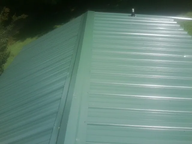 New green metal panels meeting at the ridge of a roof — Flat Roof Repair work by our crew in Waupun