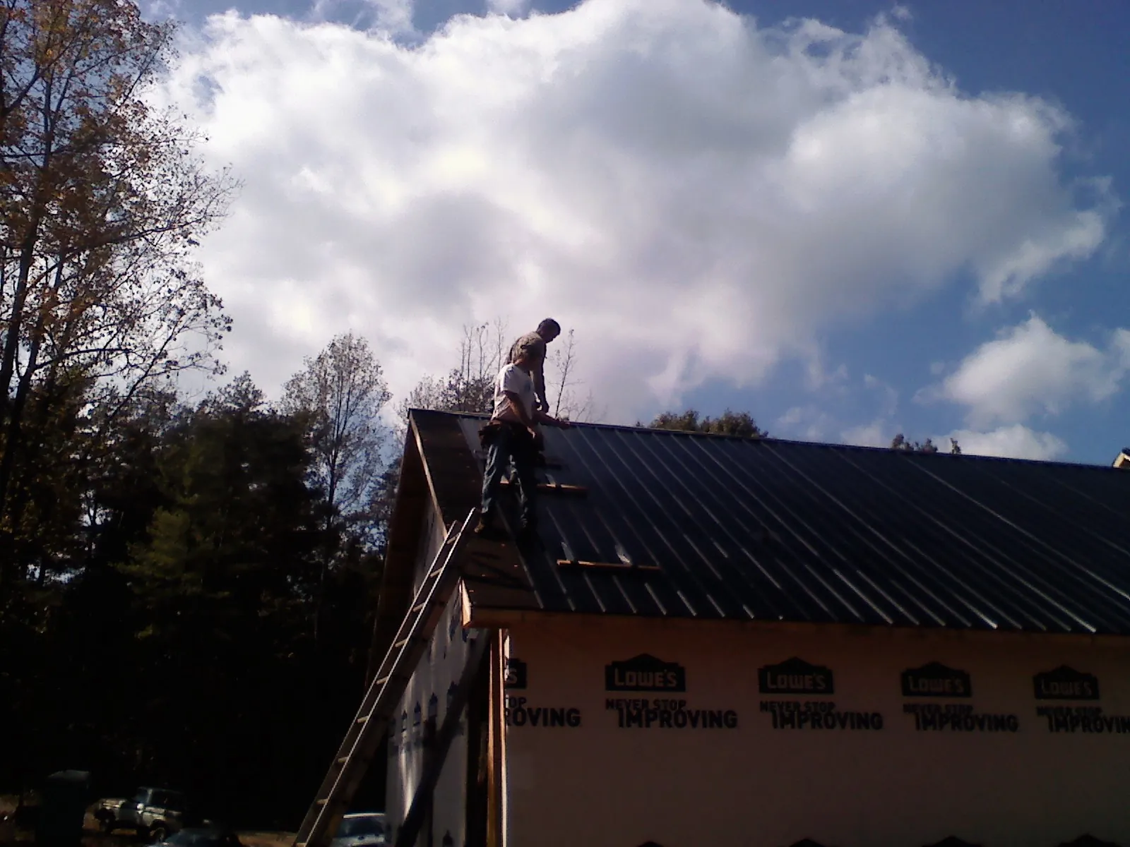 Roofer fastening dark metal panels high against a cloudy sky, from a Roof Inspection job in Waupun