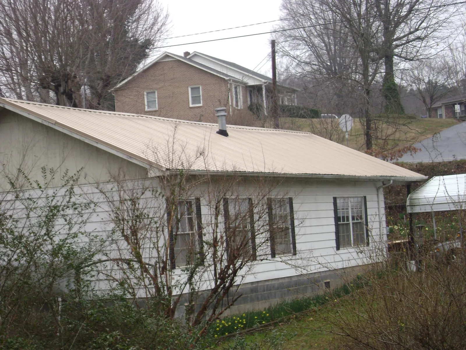 Tan metal roof on a white sided house set into a hillside — Commercial Roofing by Roofing Brothers in Waupun