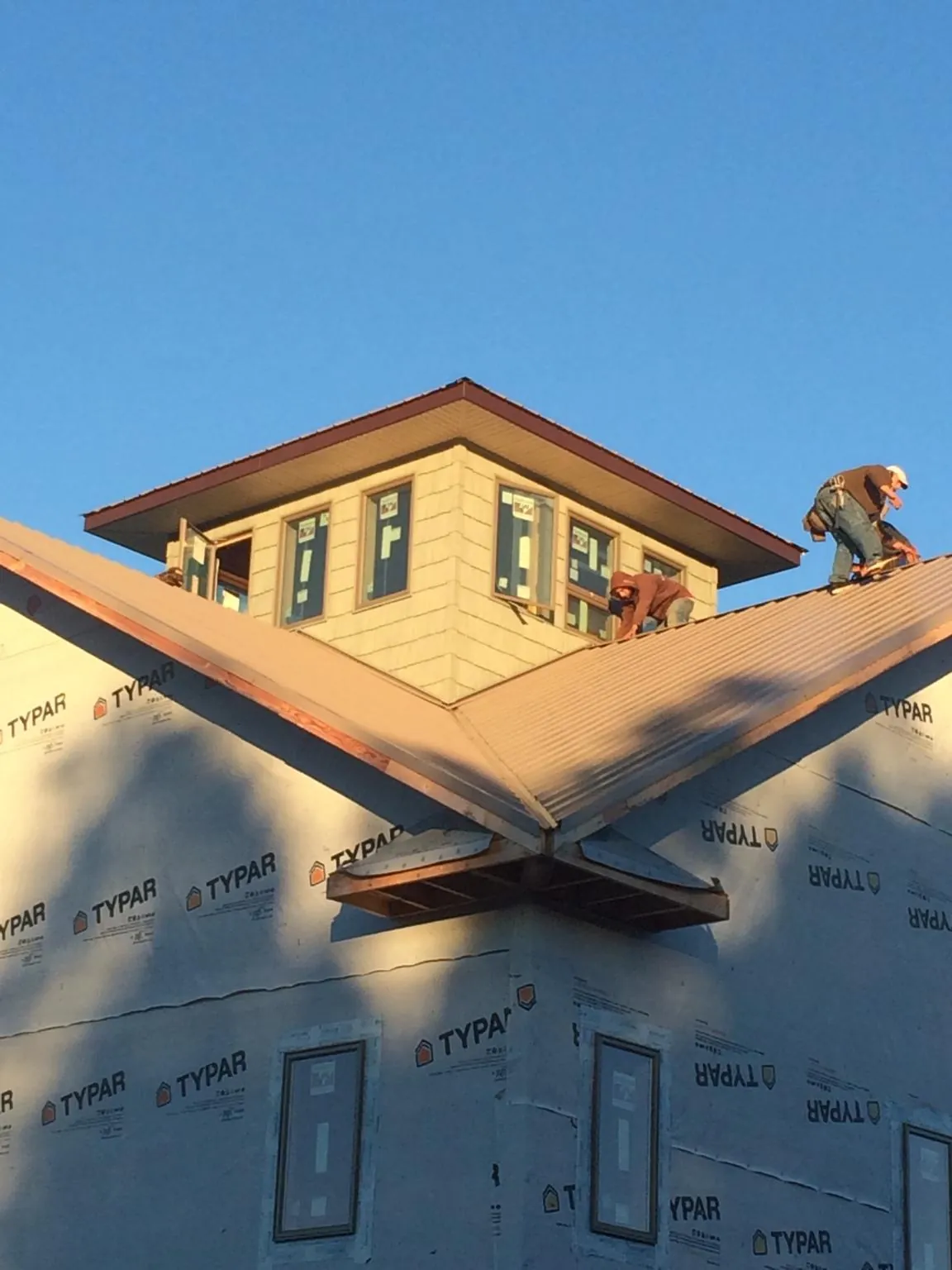 Roofers working around a rooftop cupola on a new metal roof at sunset — Roof Waterproofing in Waupun by Roofing Brothers